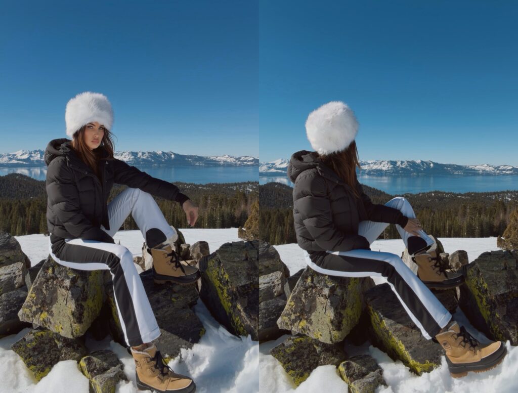 Misha Skova in a black puffer jacket, La Carrie faux fur hat, and tan boots sits on mossy rocks in a snowy Lake Tahoe landscape of with a lake and snow-capped mountains under a clear blue sky.